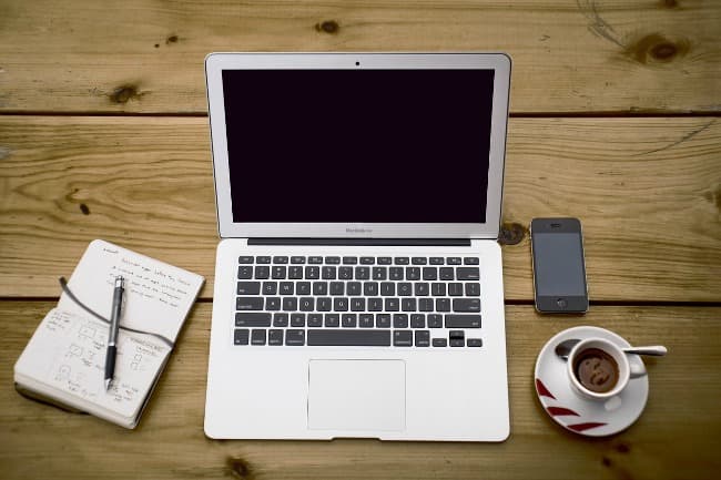 Laptop, notebook, cell phone and cup of coffee arranged on wooden table
